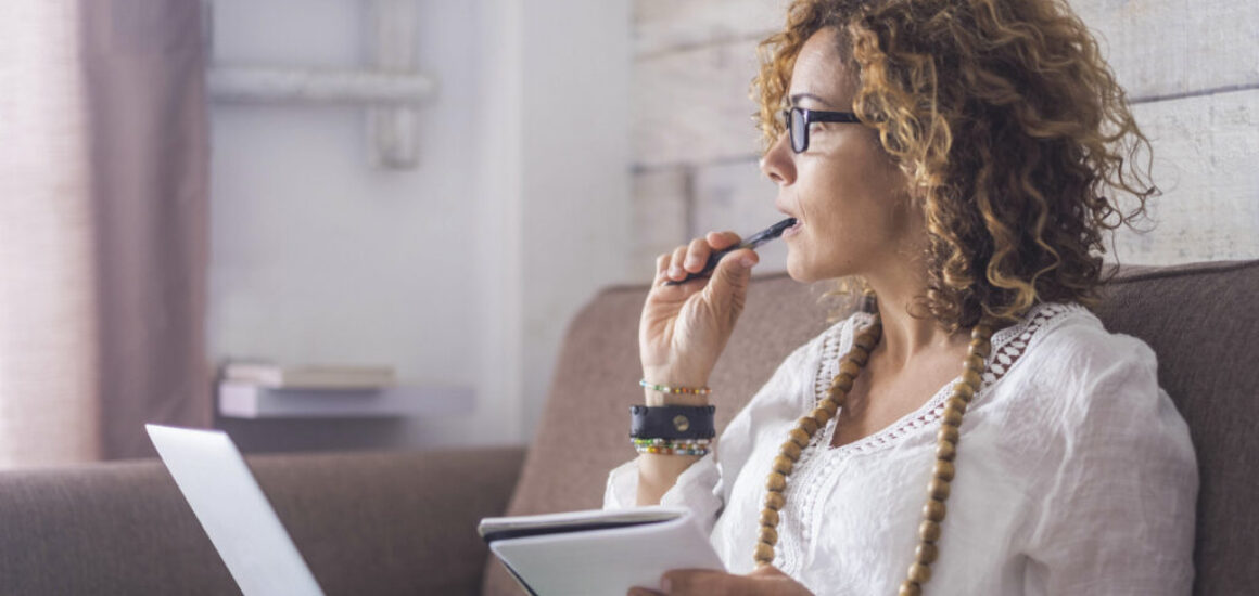 Woman thinking about why she can't decorate while chewing on her pen and staring out the window